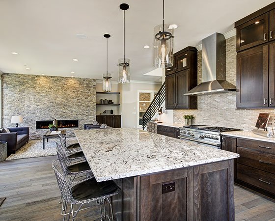 Modern kitchen with dark brown cabinets, large island with quartz countertop, metal chairs, and warm lighting.