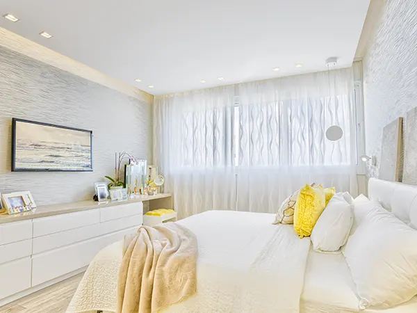 A white bedroom with yellow pillow and white covers