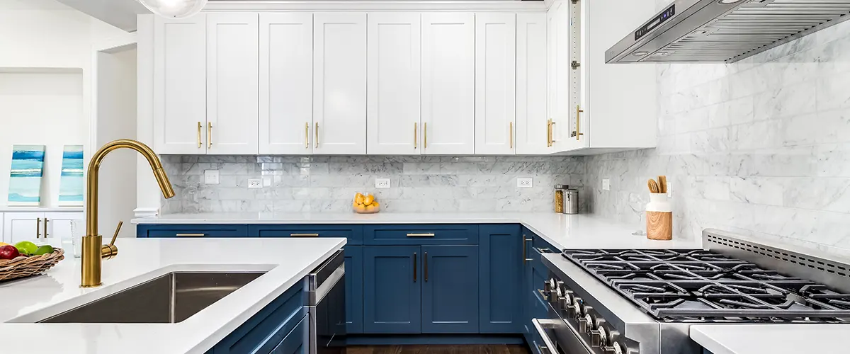 White upper cabinets with golden pulls and blue base cabinets with black pulls