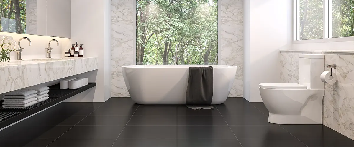 A white tub in a bathroom with black floor tiles and a white toilet