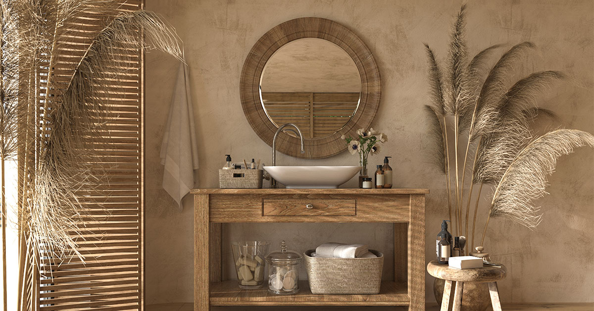 A light brown bathroom with a simple vanity, round mirror, and dry plants