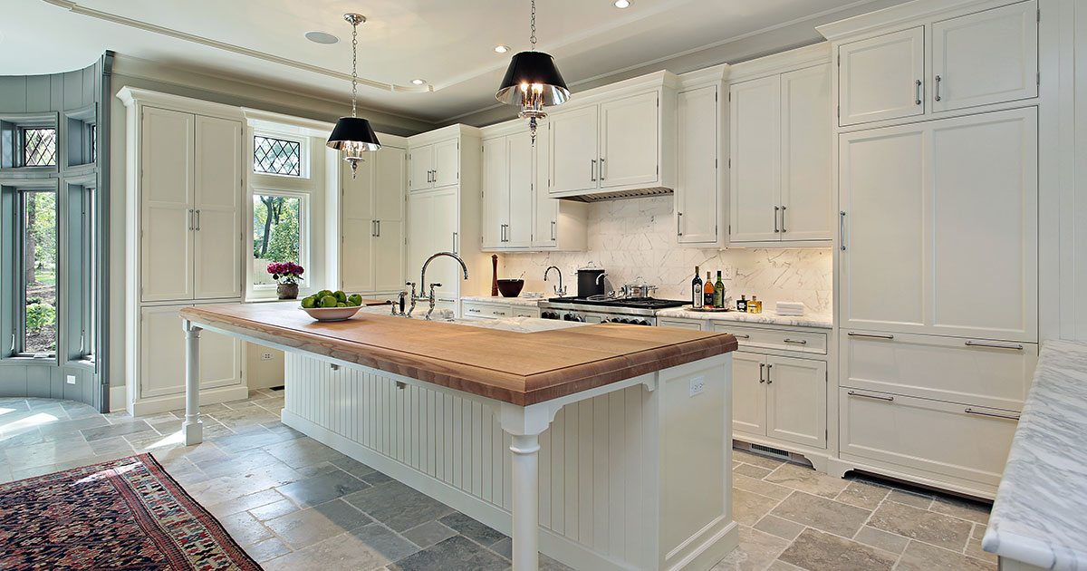 A kitchen with white cabinets and black hardware and an island with wooden countertop