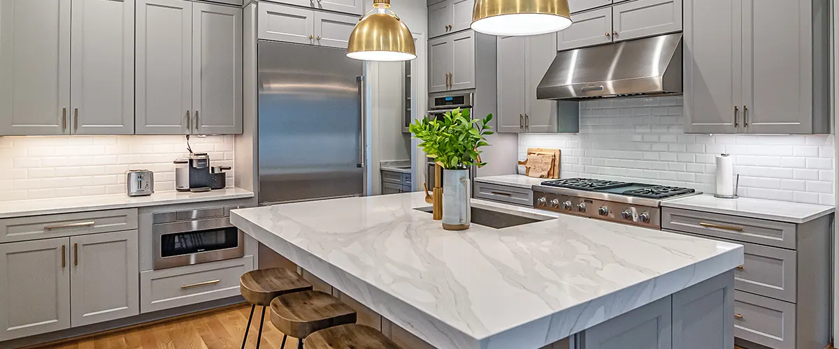 A kitchen with gray cabinets, golden lights and marble countertop