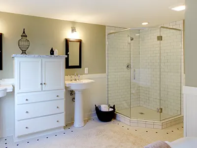 A glass shower with two pedestal sinks separated by a cabinet