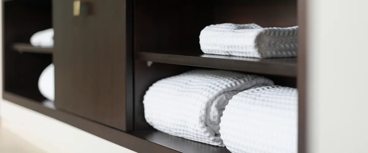 A black cabinet with open shelves used to store some white towels