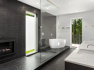 A large bathroom with dark tile flooring, a shower glass, and a freestanding tub