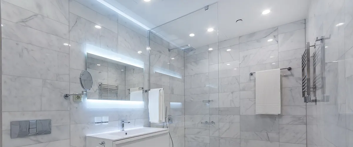 A white bathroom with glass walk-in shower and lights on ceiling