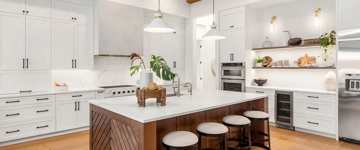 A white kitchen with wooden flooring, white cabinets, and marble countertops