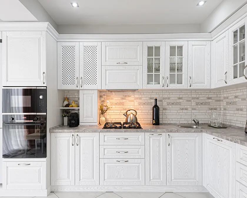 A kitchen with white cabinets with glass doors and tile backsplash