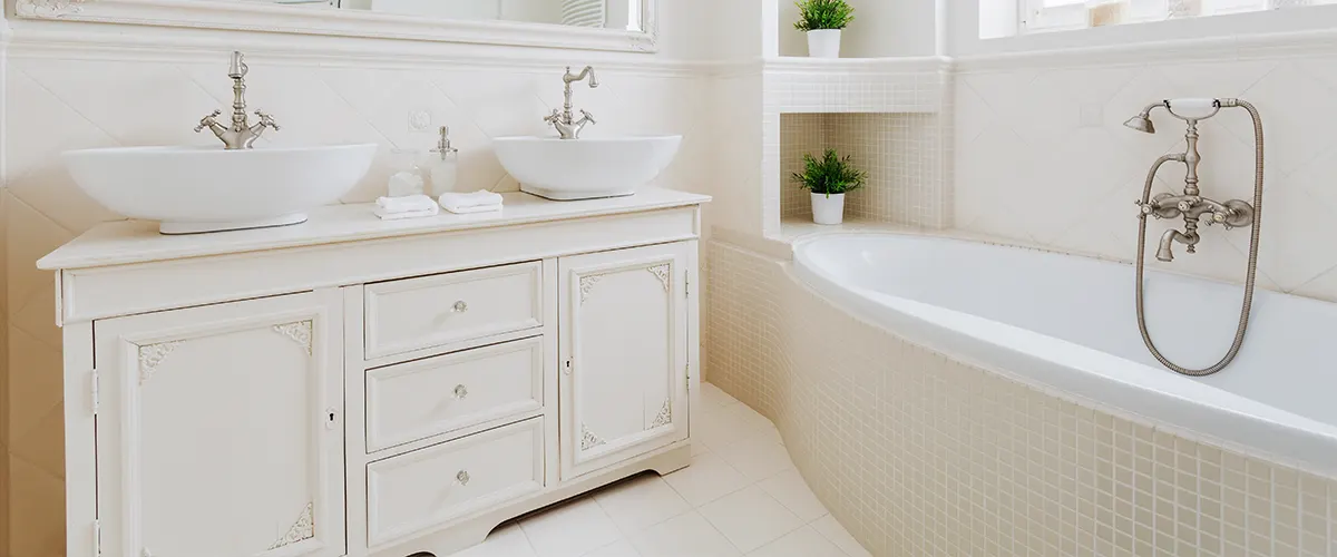 A white vanity and small tiles for a tub