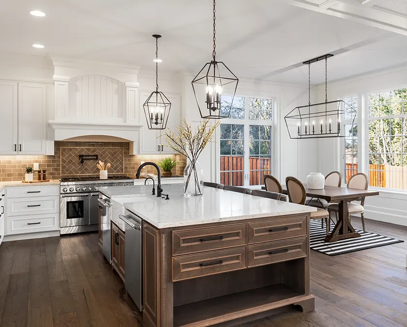 A wooden island with white marble countertop in a white kitchen with wood flooring