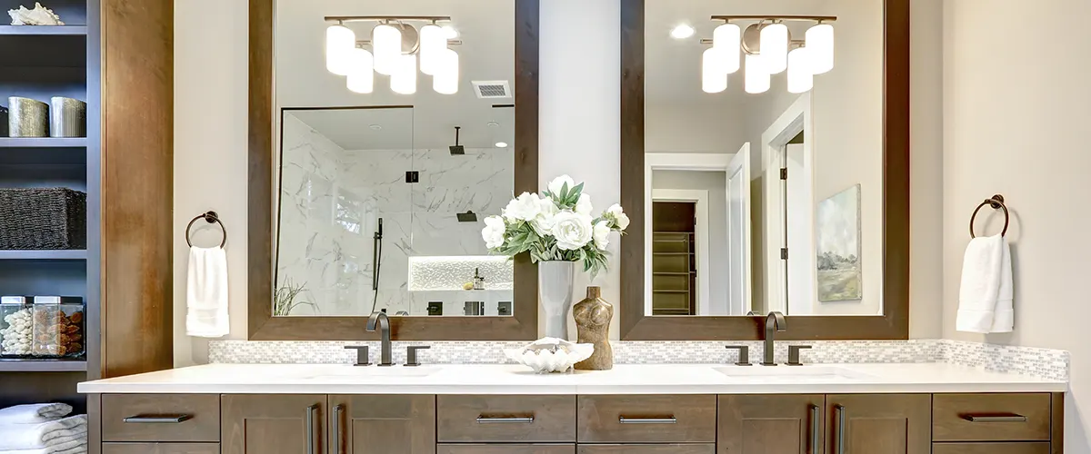 A bathroom with sconces and overhead lights reflected in a bathroom mirror