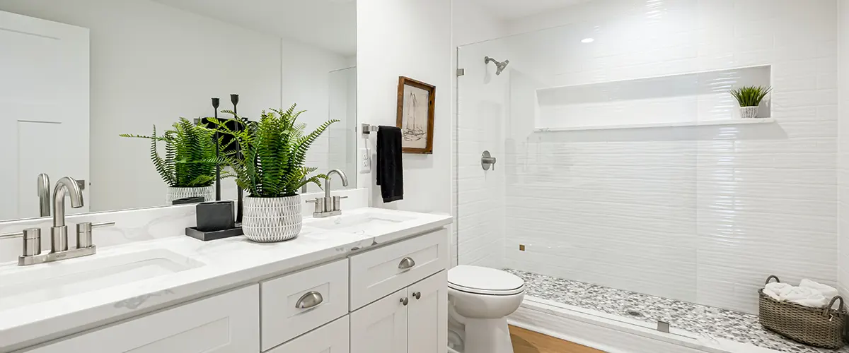 A white bathroom with a plant, vanity, toilet, and shower