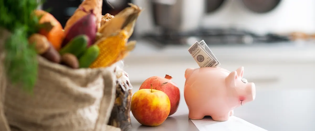 A sack of fruits and vegetables and a piggy bank with a dollar in it to prepare for a kitchen remodel