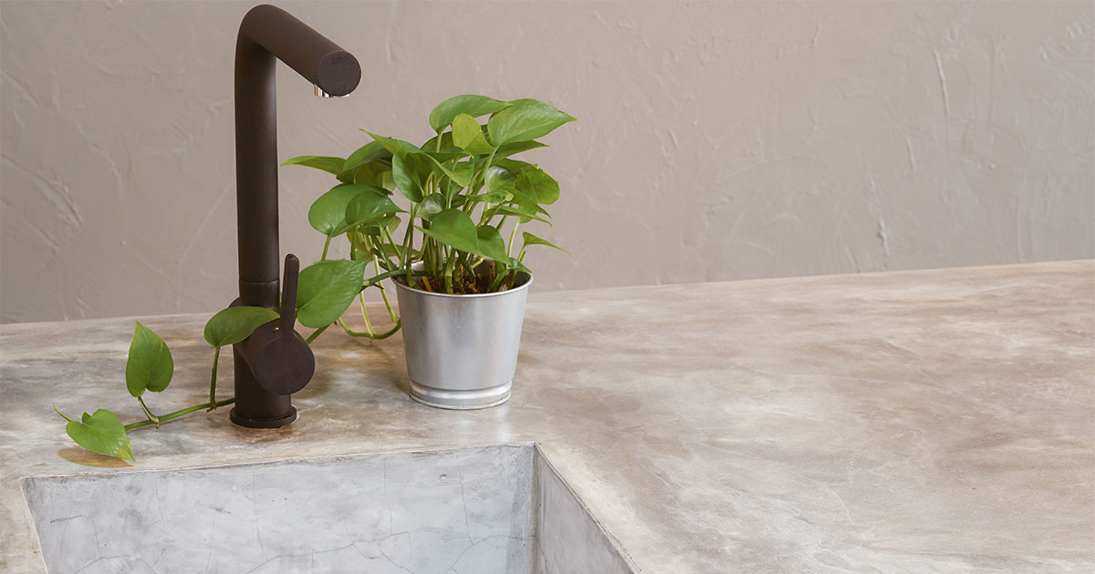 A concrete countertop with a black faucet and a plant in a bucket