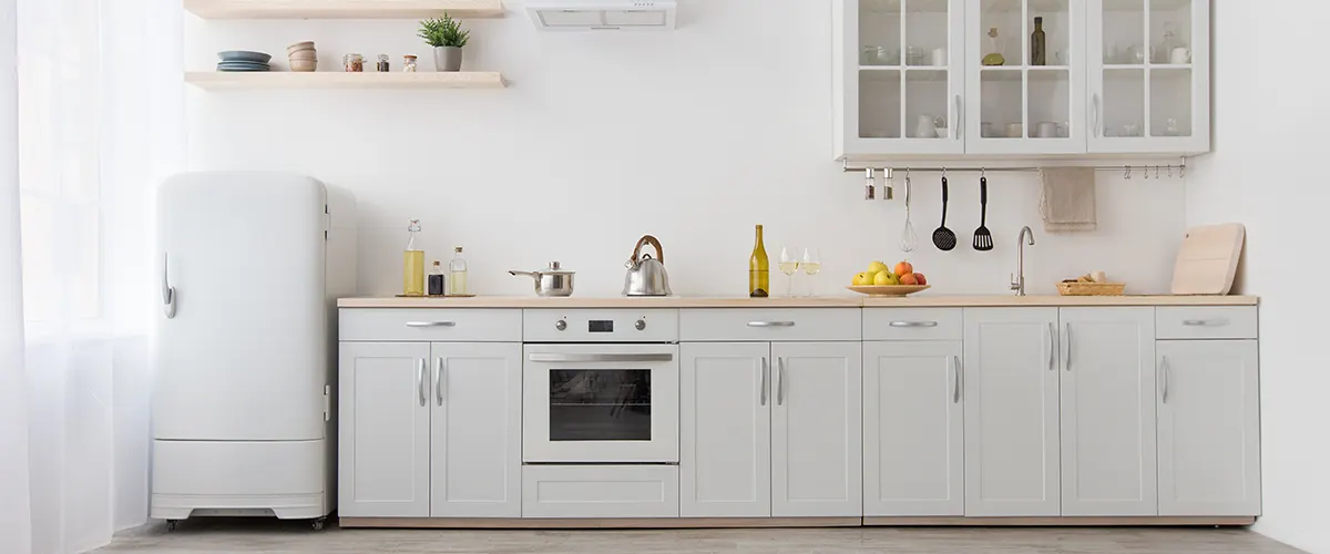 A beautiful white kitchen with silver hardware on cabinets and a vintage fridge