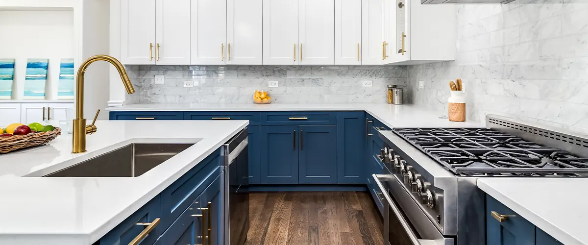 A beautiful kitchen with white upper cabinets and dark blue base cabinets with golden hardware