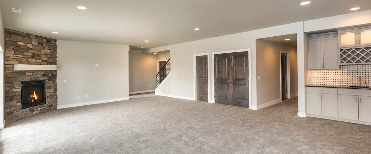 A basement with carpet flooring with fireplace and kitchenette